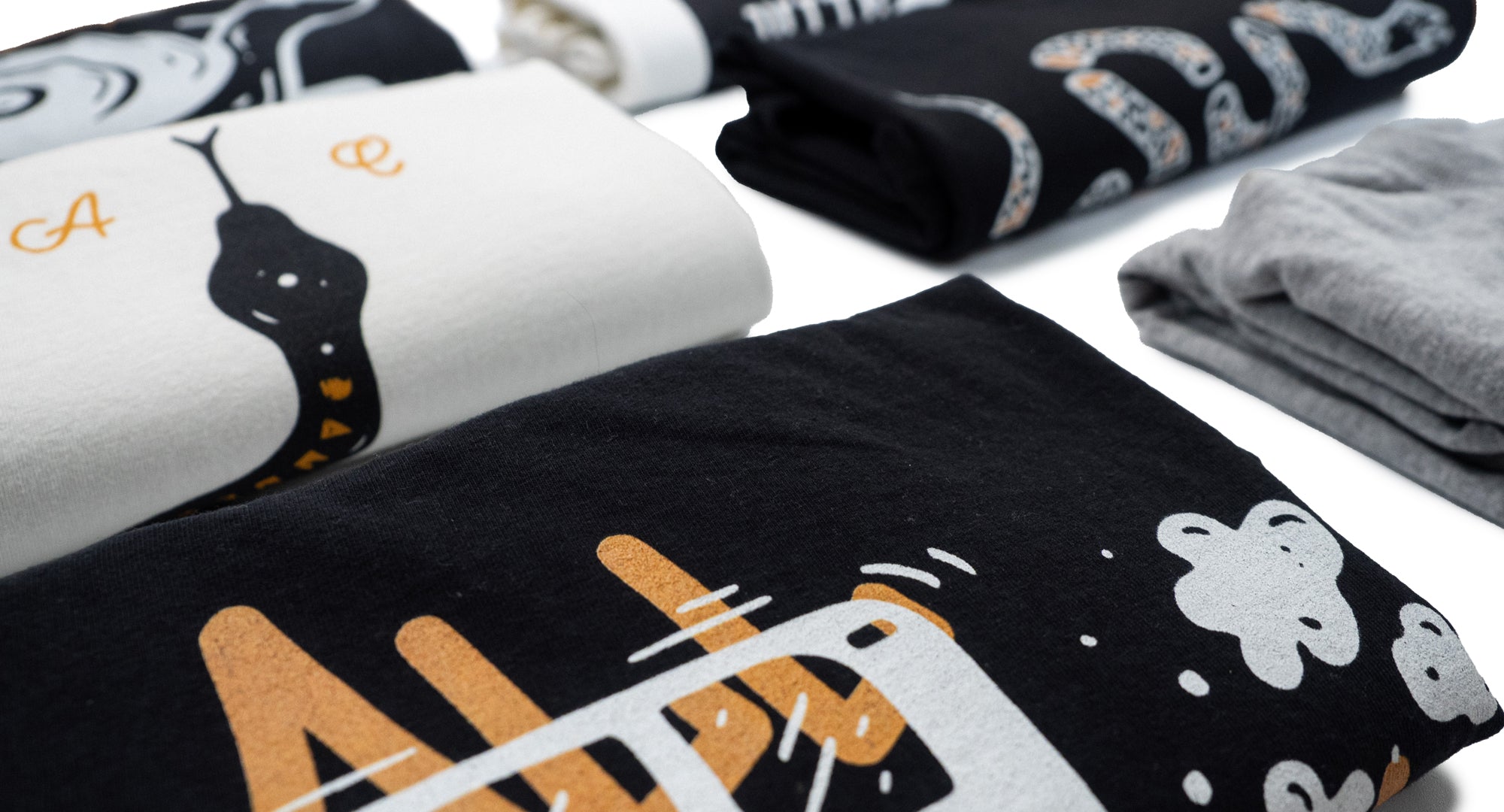 Folded AUC heavyweight t-shirts with various designs on a white surface